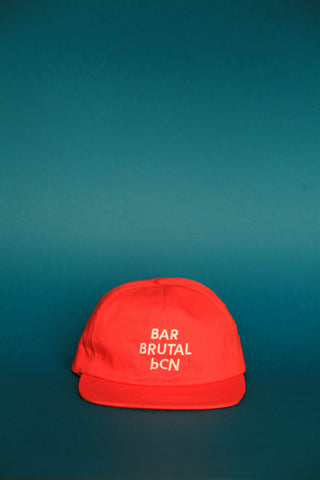 A bright red baseball cap with white embroidered text reading 'BAR BRUTAL bCN' on the front, set against a dark teal gradient background.