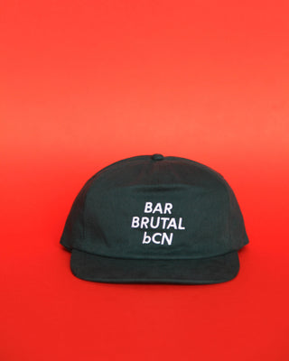 A dark green flat-brim cap with white embroidered text reading 'BAR BRUTAL bCN' on the front, set against a solid red background.