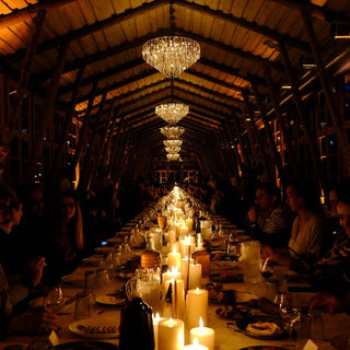 Long dining table set for a formal dinner with candles and glasses under a high wooden ceiling.